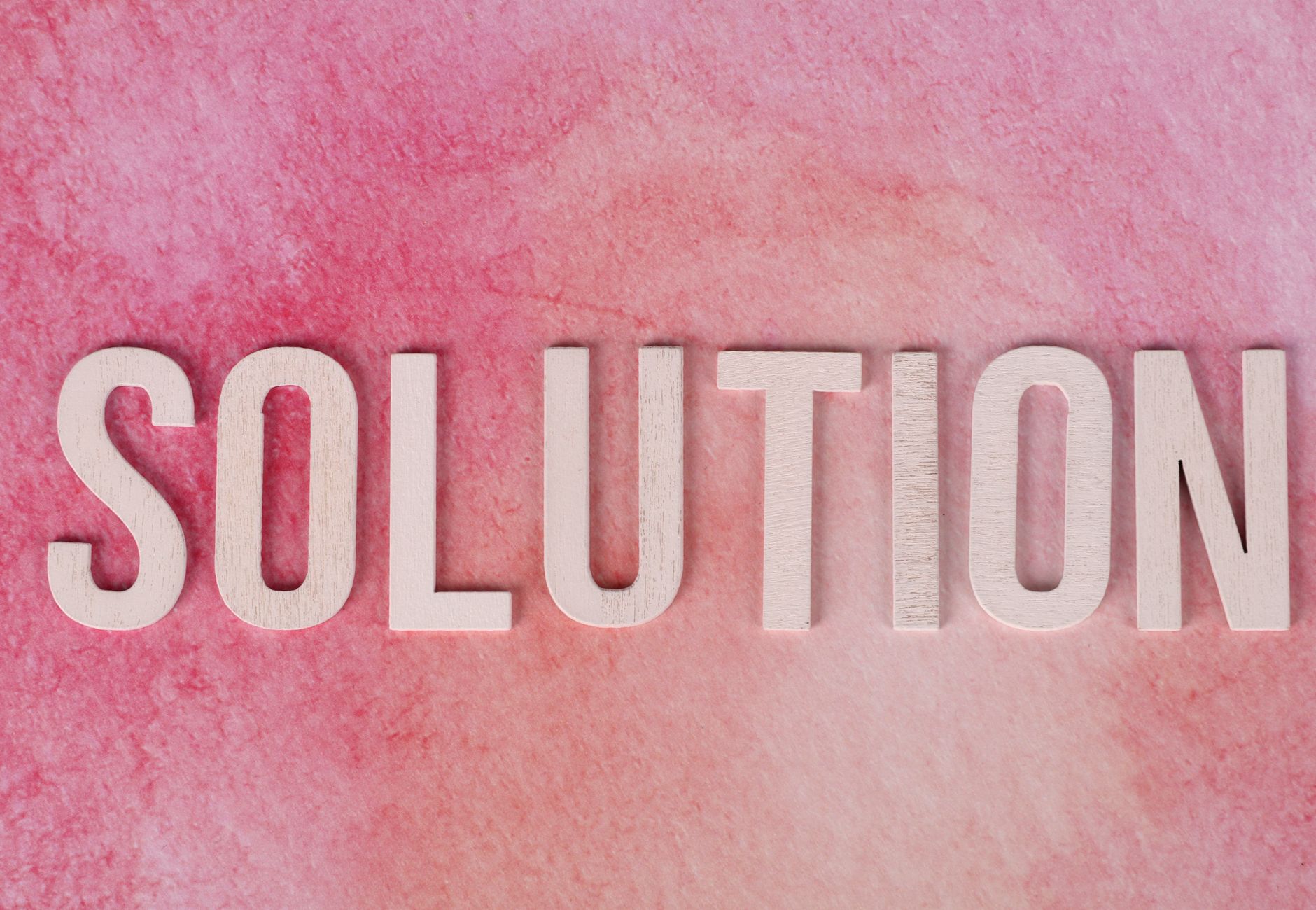 Wooden letters spelling 'Solution' on a textured pink background.