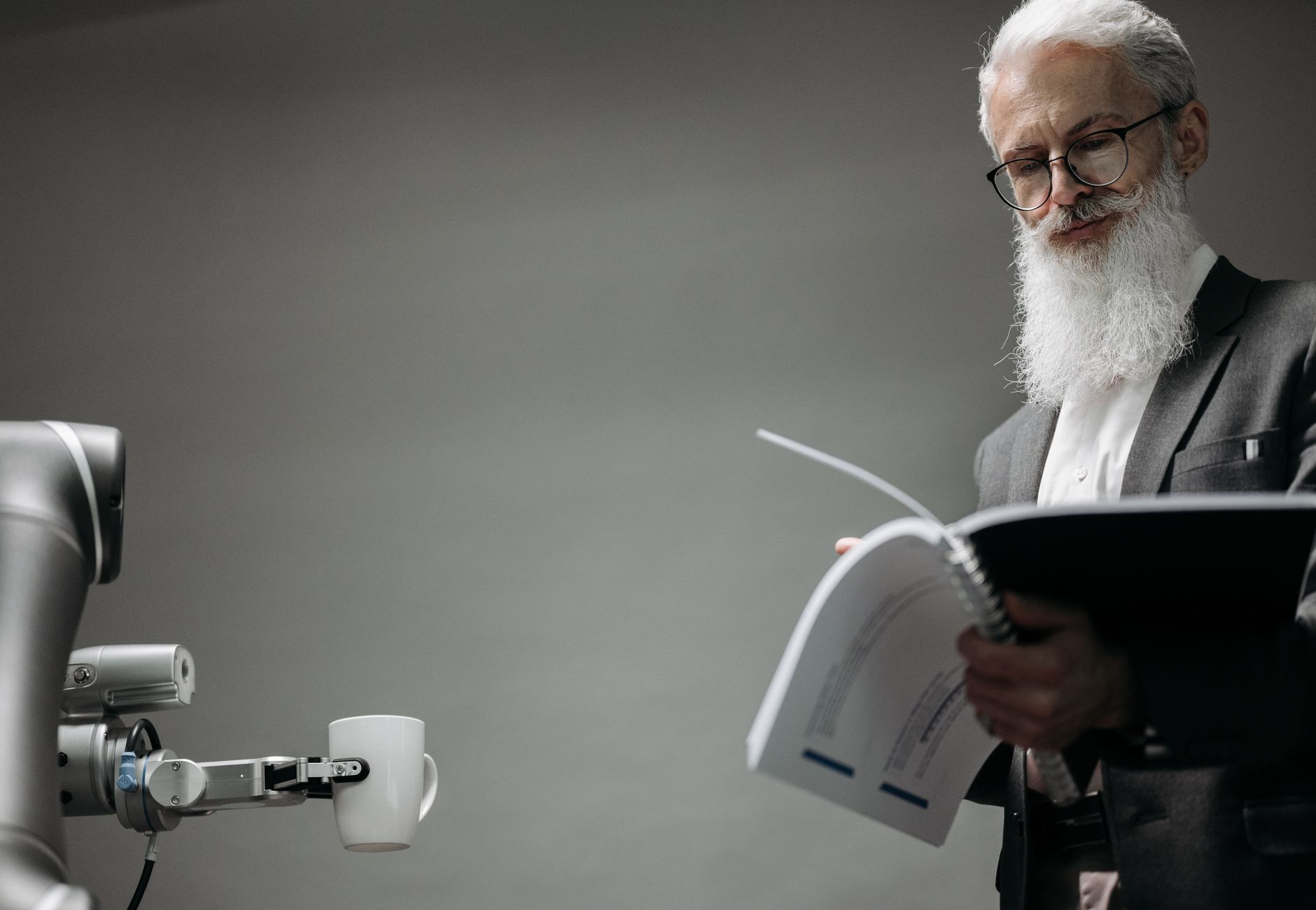 Elderly man reads as a robotic arm holds a coffee cup, showcasing technology integration.
