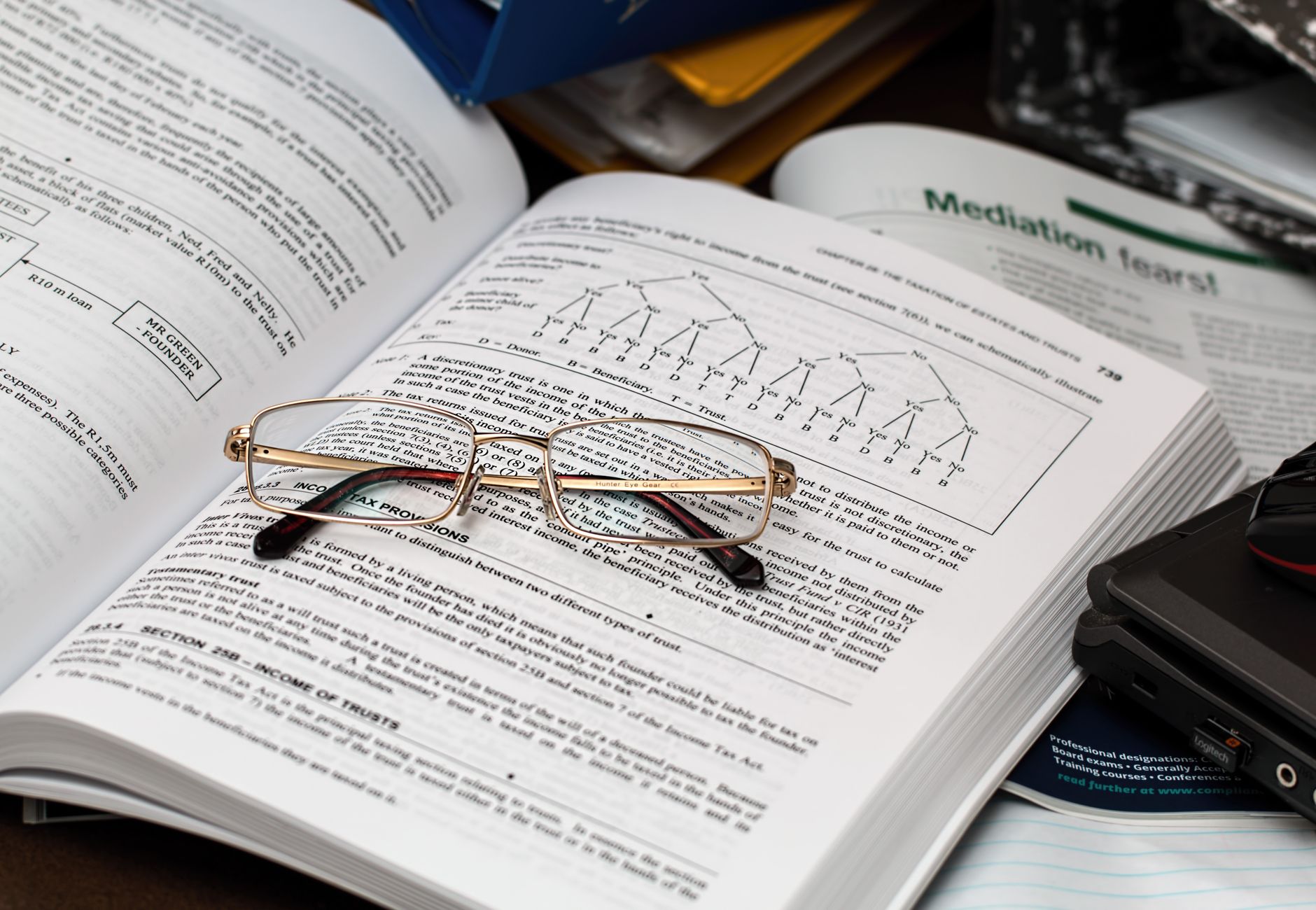 An open book with reading glasses, surrounded by study materials and a laptop, ideal for education themes.