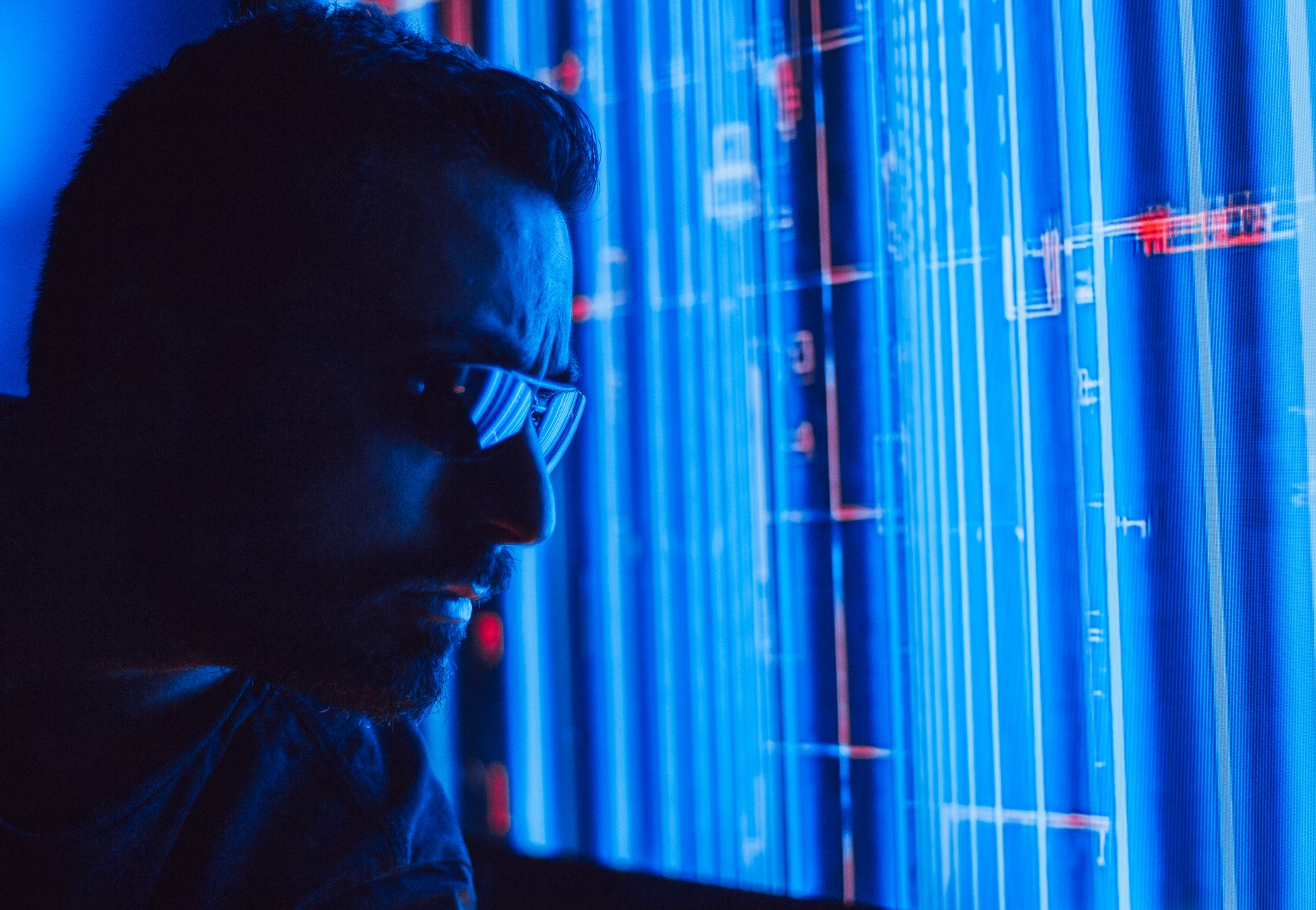 A man in sunglasses intently studies a vibrant blue holographic screen, symbolizing digital technology.